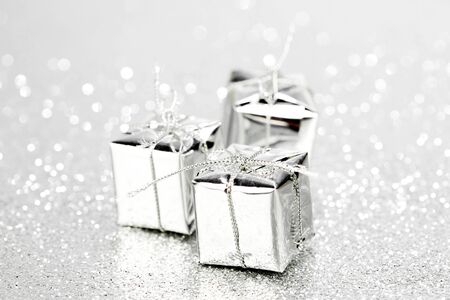 Decorative silver boxes with holiday gifts on shiny glitter background