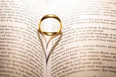 One golden wedding ring on Holy bible book with heart shaped shadow close upの写真素材
