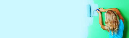 Young woman paints her appartment walls from green to blue using paint roller , copy space for text