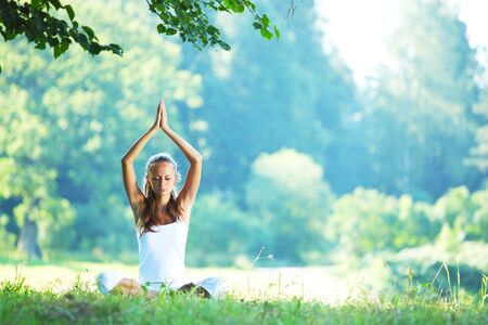 Yoga woman in white on green park grass in lotus asana poseの写真素材