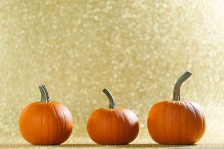 Three Pumpkins on golden glittery background with bokeh lights and copy spaceの写真素材