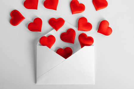 Valentine day love letter, envelope of craft paper with red hearts heap spread on white background.の写真素材