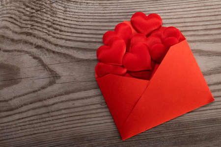 Valentine day love letter, envelope of craft red paper with red hearts heap spread on wood...