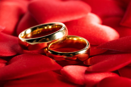 Two golden wedding rings on red satin hearts background