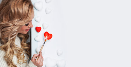 Happy smiling young woman painting red decorative heart on white background Valentines day card decorationの写真素材