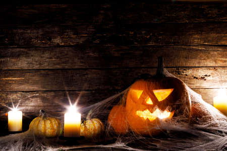 Festive mystical halloween interior. Pumpkin, spider web, burning candles, spiders on dark wooden backgroundの写真素材