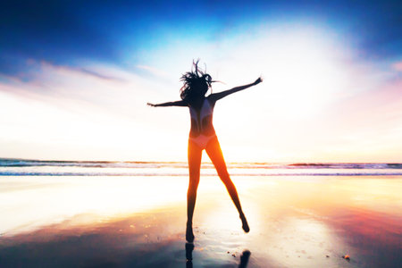 Woman jumping on tropical beach at sunset, sea on backgroundの写真素材