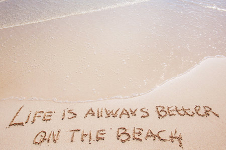 Life is always better on the beach written on the sand of tropical sea beachの写真素材