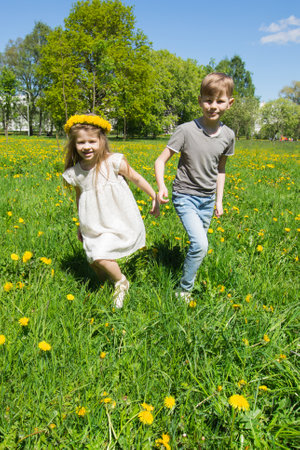 Happy children friends run and play outdoors on yellow dandelion flower meadowの写真素材