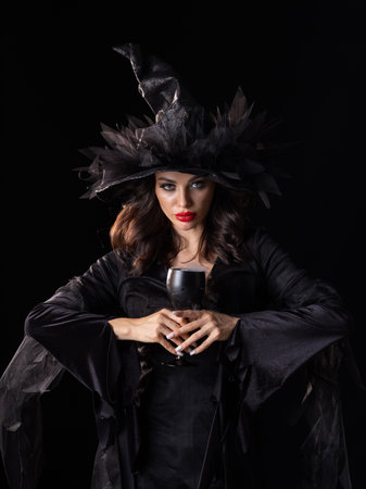 Beautiful sorceress woman in Halloween witch costume dress put a spell smoke in hands isolated on black backgroundの写真素材