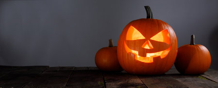 Glowing Halloween pumpkin head jack lantern on wooden table over gray background with copy space for textの写真素材