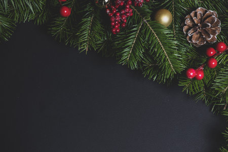 Christmas Border frame of tree branches and red berries on black paper background flat lay top view...