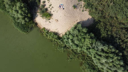 Top view of an abandoned sandy beach with vegetation around and a green lake