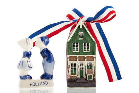 Old Dutch canal house with a red-white-blue ribbon knotted in a bow next to kissing old Dutch farm kids, all isolated over a white の写真素材