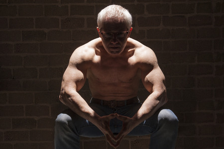 Muscular man with sinister look sitting topless in spotlightの写真素材