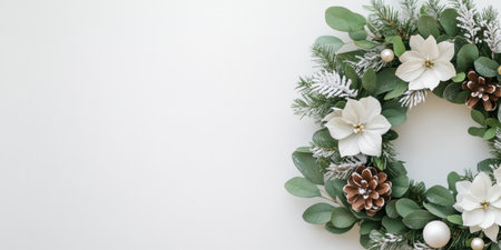 Elegant winter holiday wreath with white flowers, pinecones, frosted leaves, and evergreen foliage on a light minimalist background.の素材