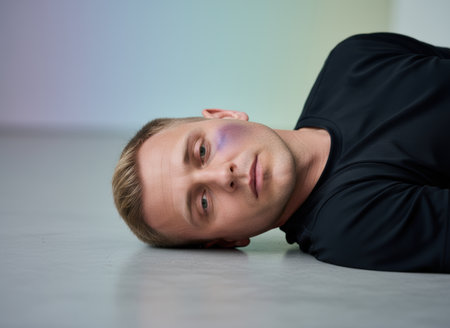 Young man with bruised face lying on the floor, close up portrait showing expression of pain and vulnerability in soft lighting.の素材