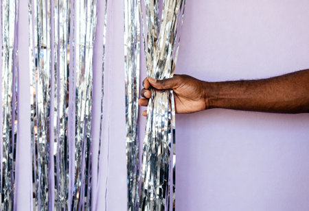 Hand pulling silver metallic streamers against a pastel purple background, highlighting festive party decor and celebration details.の素材