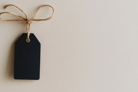 Minimalist black gift tag with twine on beige background for elegant labeling and customization needs.の素材