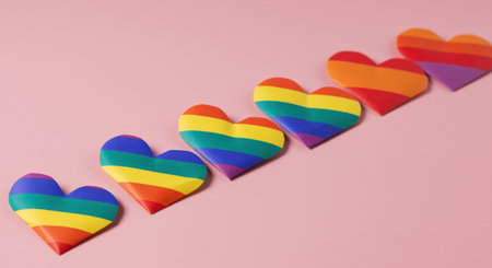 Rainbow paper hearts arranged in a row on a pink background symbolizing lgbtq pride, love, acceptance, and diversity.の素材