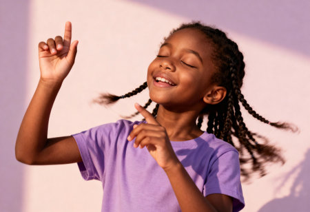 Joyful young girl dancing with braids and smiling in sunlight, wearing a purple shirt against a softly lit pastel background.の素材