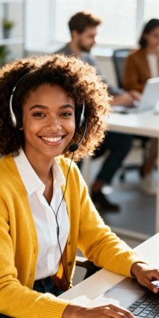 Young professional woman with headset providing customer support in modern office environment with coworkers in background.の素材