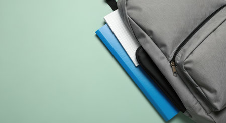 Gray backpack with notebooks and folders on pastel green background, organized school supplies ready for academic or college use.の素材