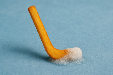 Creative food concept with single french fry shaped like a hockey stick and covered with coarse salt on blue background.の素材