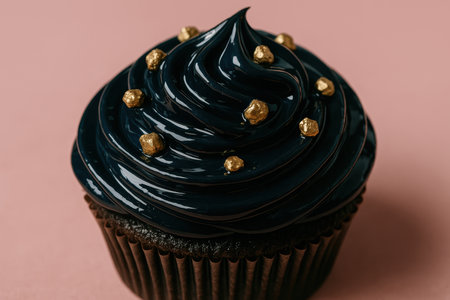 Decadent chocolate cupcake with glossy black frosting and gold decorative pearls on pastel pink background, close up dessert concept.の素材