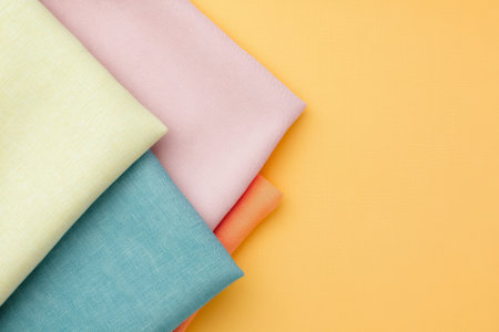 Colorful textile fabrics in pastel shades arranged against a bright yellow background, showcasing texture and material variety.の素材