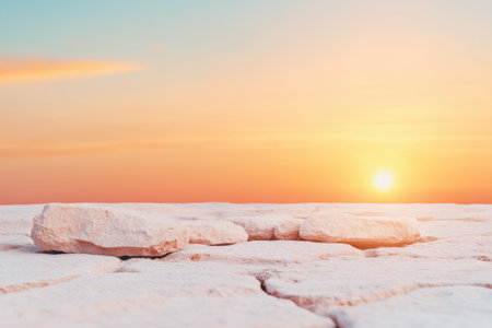 Peaceful desert landscape at sunset with cracked earth and scattered rocks under a vibrant sky.の素材