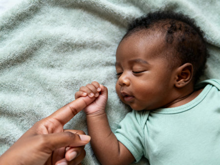 Peaceful newborn baby holding adult's finger while sleeping on soft blanket, tenderness and bonding in early parent child relationship.の素材
