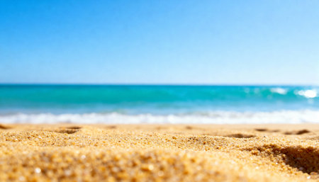 Golden sandy beach stretching under bright sunlight with clear blue sky and calm ocean waves in the distance.の素材