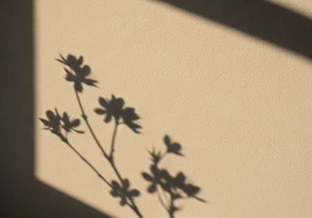 Delicate flowers casting soft natural shadows on a beige wall as sunlight filters through a window, creating a minimalist scene.の素材