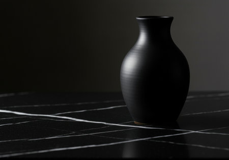 Minimalist black ceramic vase on dark marble surface with white veining in modern moody lighting and elegant composition.の素材