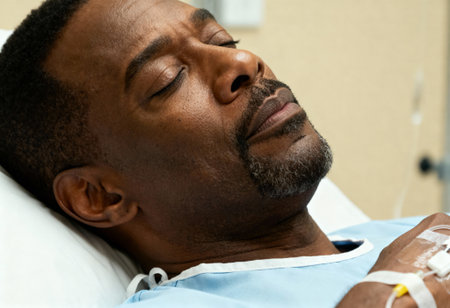 Middle aged man resting in hospital bed with closed eyes, peaceful facial expression, medical gown and wristband visible.の素材