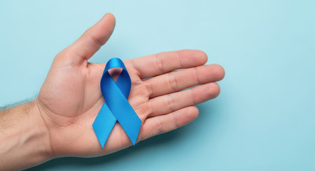 Male hand holding blue awareness ribbon on pastel background symbolizing support, hope and health disease prevention campaign.の素材
