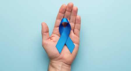 Male hand holding blue awareness ribbon on pastel background symbolizing health support solidarity and medical charity campaign.の素材