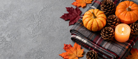 cozy autumn arrangement with pumpkins, pine cones, plaid blanket, candle and colorful leaves on textured gray background.の素材