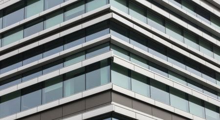 Modern glass office building exterior with reflective windows forming geometric architectural lines and a sharp corner perspective.の素材