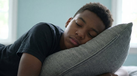 Teenage boy sleeping peacefully on a gray cushion in a quiet bedroom, resting on his side in soft daylight with a relaxed expression.の素材