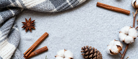 Winter cozy scene with wool blanket, cinnamon sticks, pine cones, cotton bolls, and star anise on a soft grey background.の素材