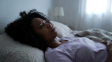 Unable to sleep at night, worried woman lying awake in bed staring at the ceiling in dark quiet bedroom with soft low light.の素材