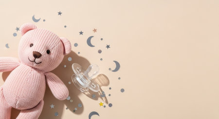 Soft pink knitted plush bear and baby pacifier on pastel background with scattered moon, star and cloud decorations for newborn theme.の素材