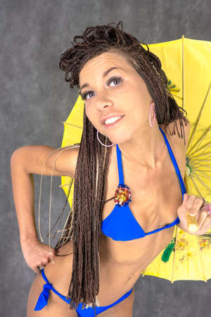 Latin American female dressed in a blue bikini with the yellow Chinese umbrella and African braidsの写真素材