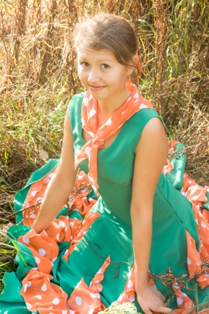 cute smiling girl sitting on the grass in a colored dressの写真素材