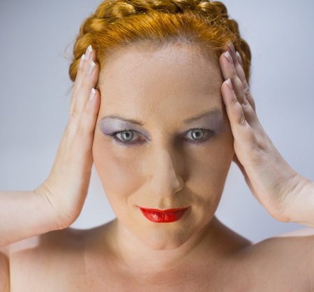 portrait of a red-haired blue-eyed woman keeps hands to templesの写真素材