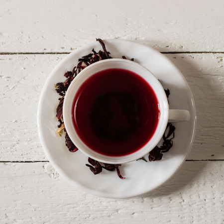 Cup of Karkadeh Red Tea with Dry Flowers on wooden tableの写真素材