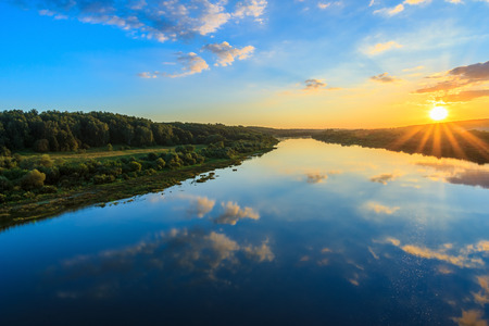sunset on the river embankment at summer evening with clouds and trees
