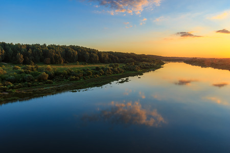 sunset on the river embankment at summer evening with clouds and trees